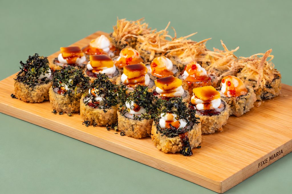 Tábua com hot rolls panados, cobertos de molho, maionese e batata palha, sobre fundo verde-salva.