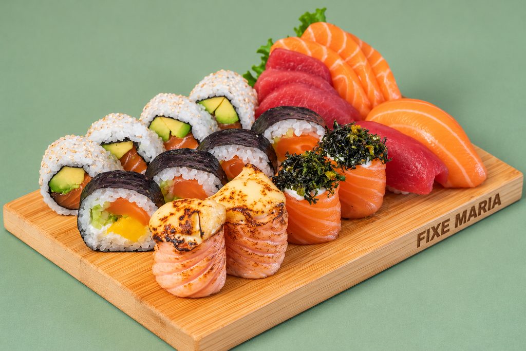 Tábua com sashimi de salmão e atum, uramaki, salmão braseado e gunkan com algas, sobre fundo verde-salva.